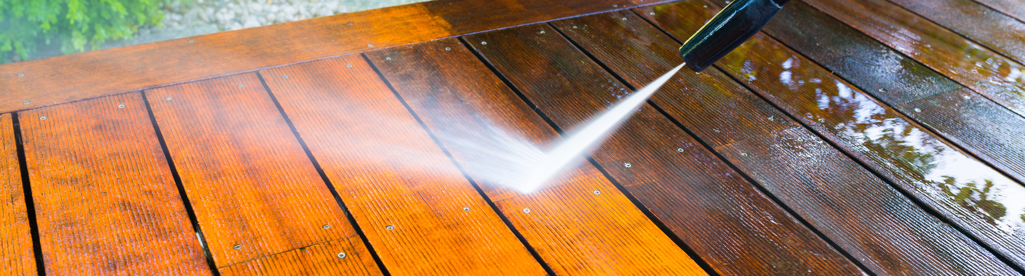 Reinigung der Terrasse mit einem Hochdruckreiniger auf der Holzoberfläche der Terrasse, sehr geringe Schärfentiefe, Schärfe auf dem Terrassenbrett unter dem Wasserstrahl.